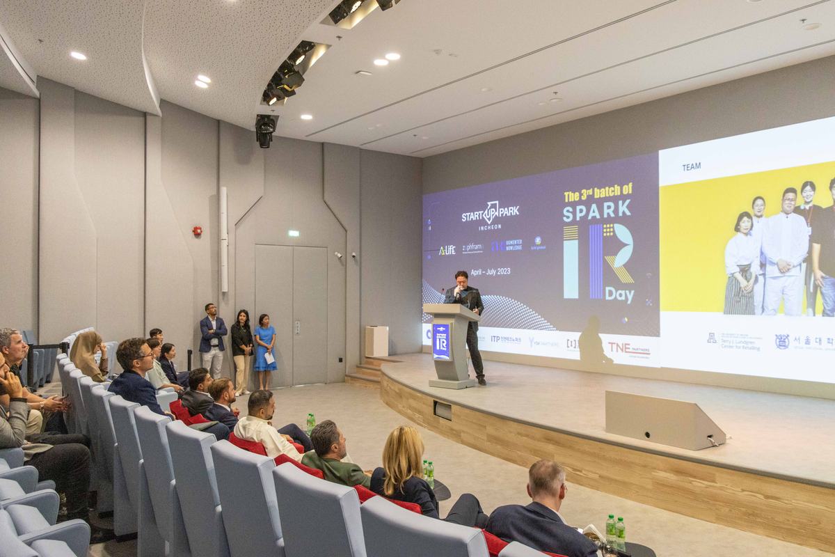 A full auditorium at SEE Institute, a speaker on stage in front of a wide screen