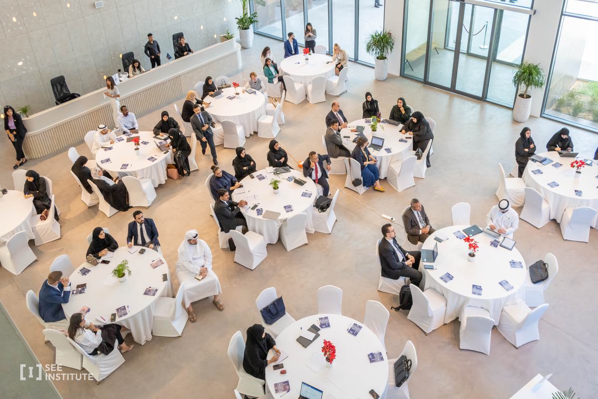 People working in groups at round tables in a daylit room at SEE Institute