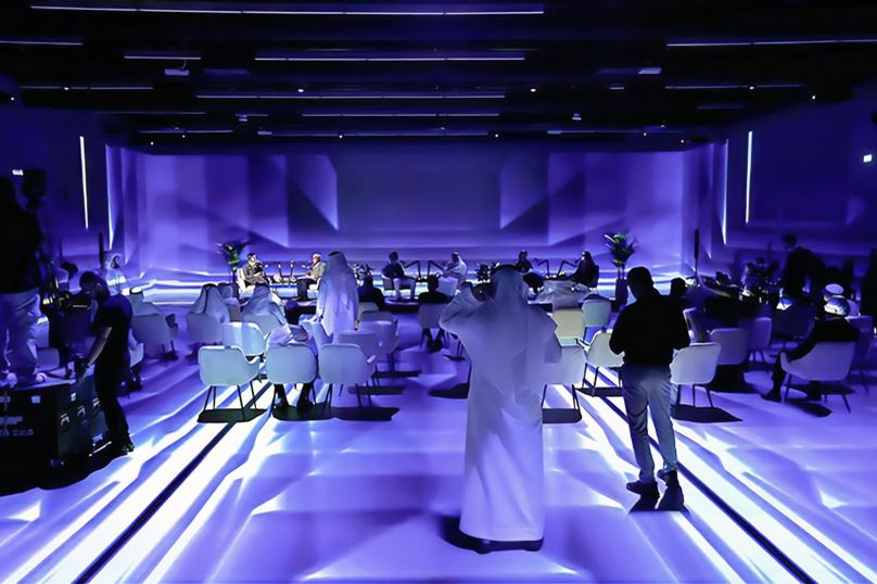 The ImmerSEE room laid out with tables and chairs, the floor and walls washed in projected violet light